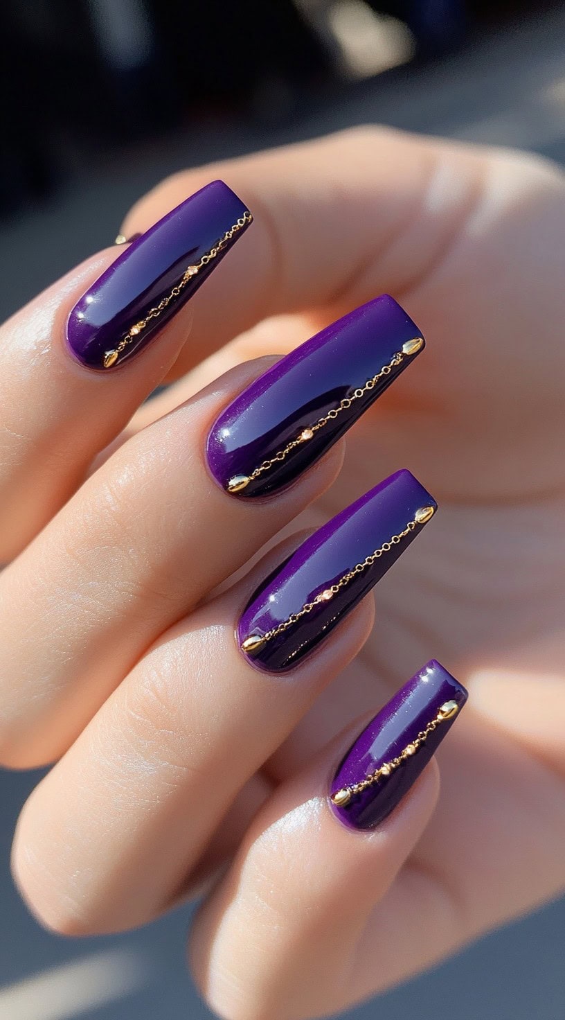 Glossy long square nails painted in rich purple, each adorned with a delicate gold chain down the center.