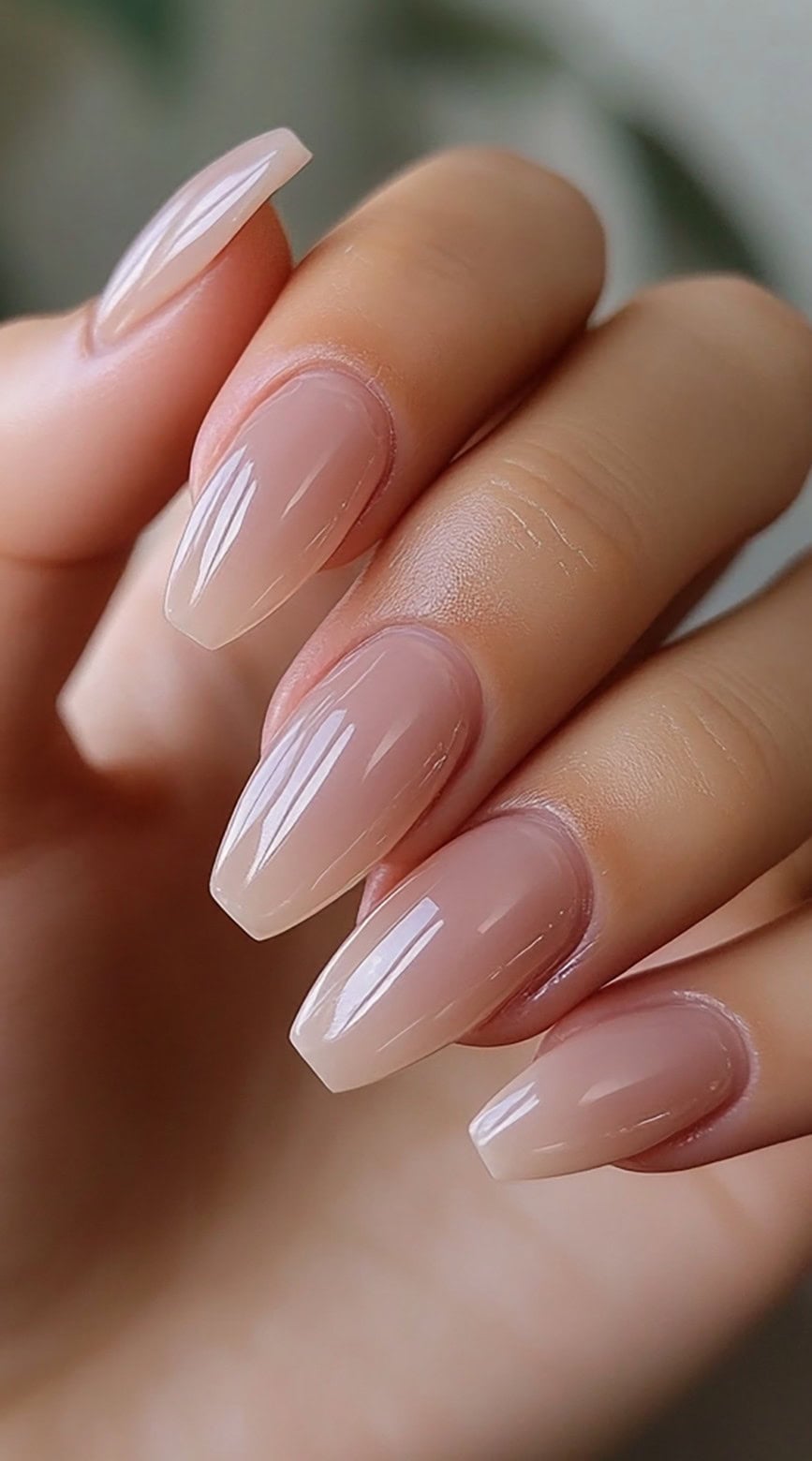 A hand with long, sculpted coffin nails in a flawless nude tone with a glossy finish.