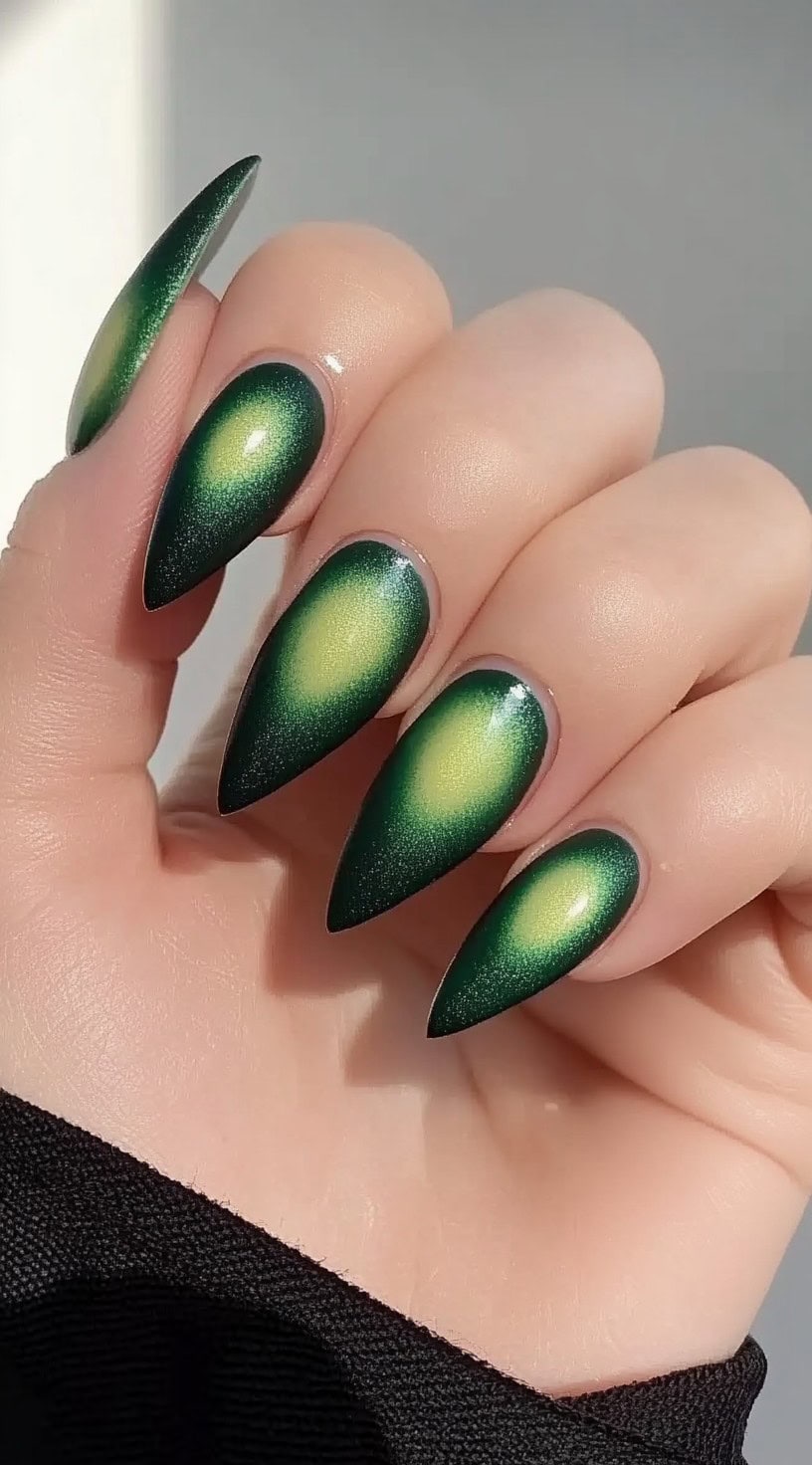 A close-up of almond-shaped nails featuring a deep green cat-eye effect with a glowing yellow-green core at the center.
