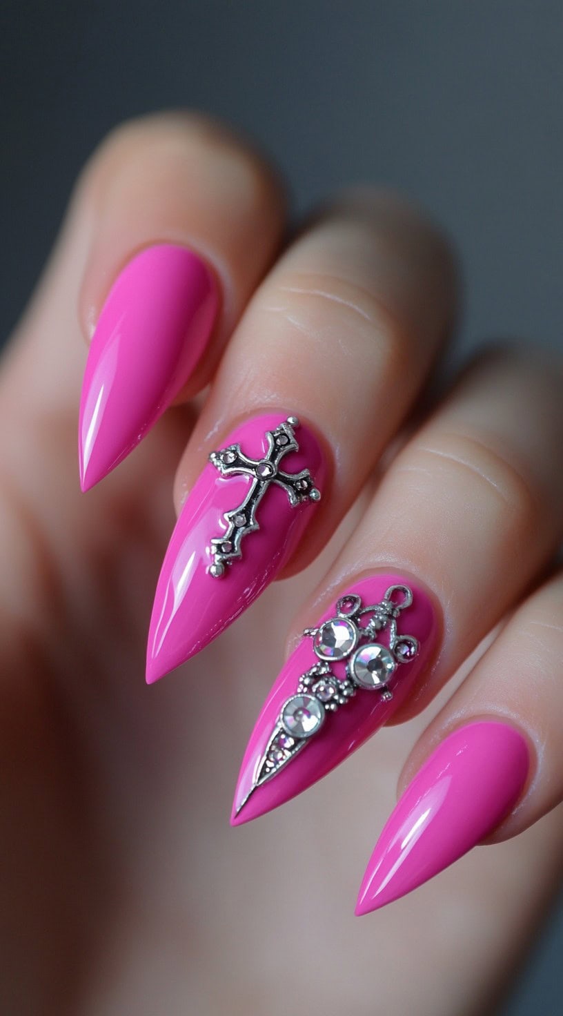 Close-up of hot pink almond nails featuring raised silver cross and jewel charms.