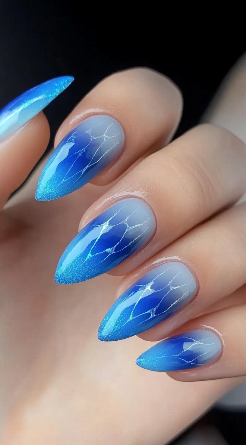 Almond-shaped nails featuring an icy blue aura ombré with delicate silver vein details resembling cracked ice.