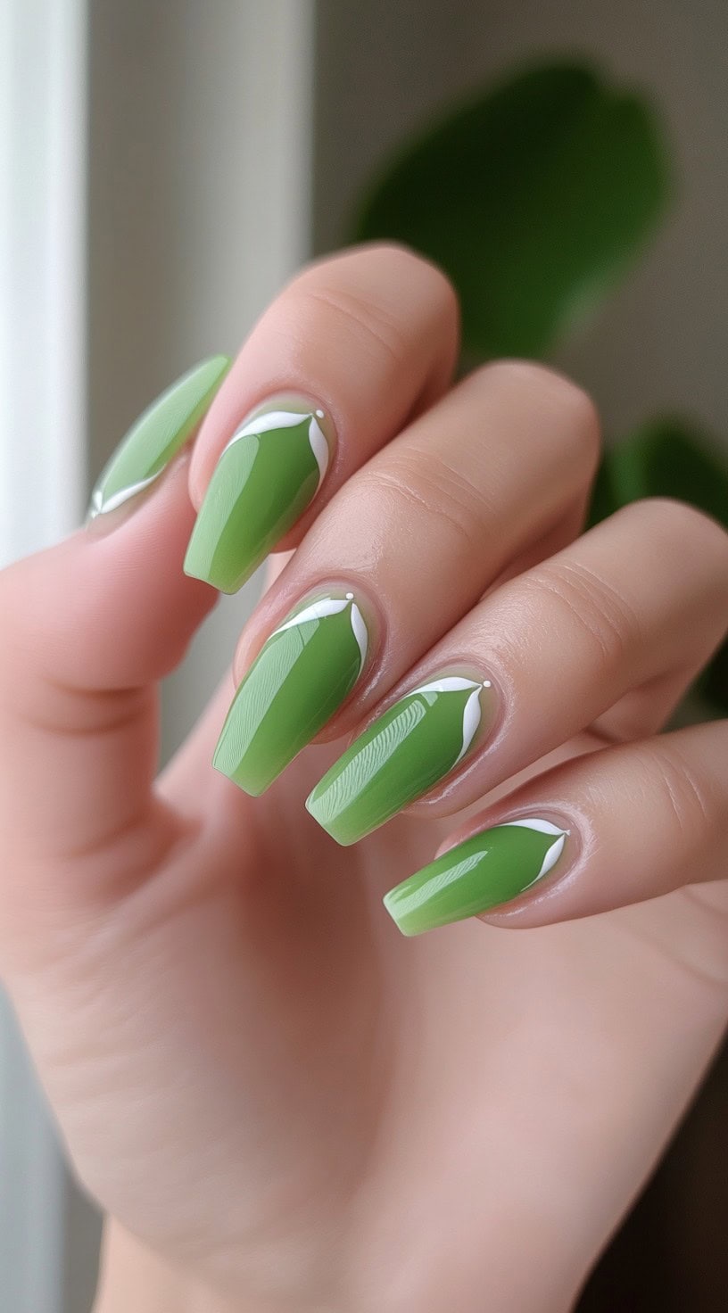Coffin-shaped nails painted in a bright matcha green with white petal-like French tips and small white dots near the cuticles.