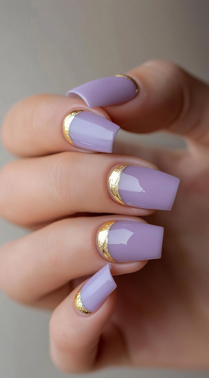 Short square lilac nails with a gold foil half-moon accent at the base of each nail.