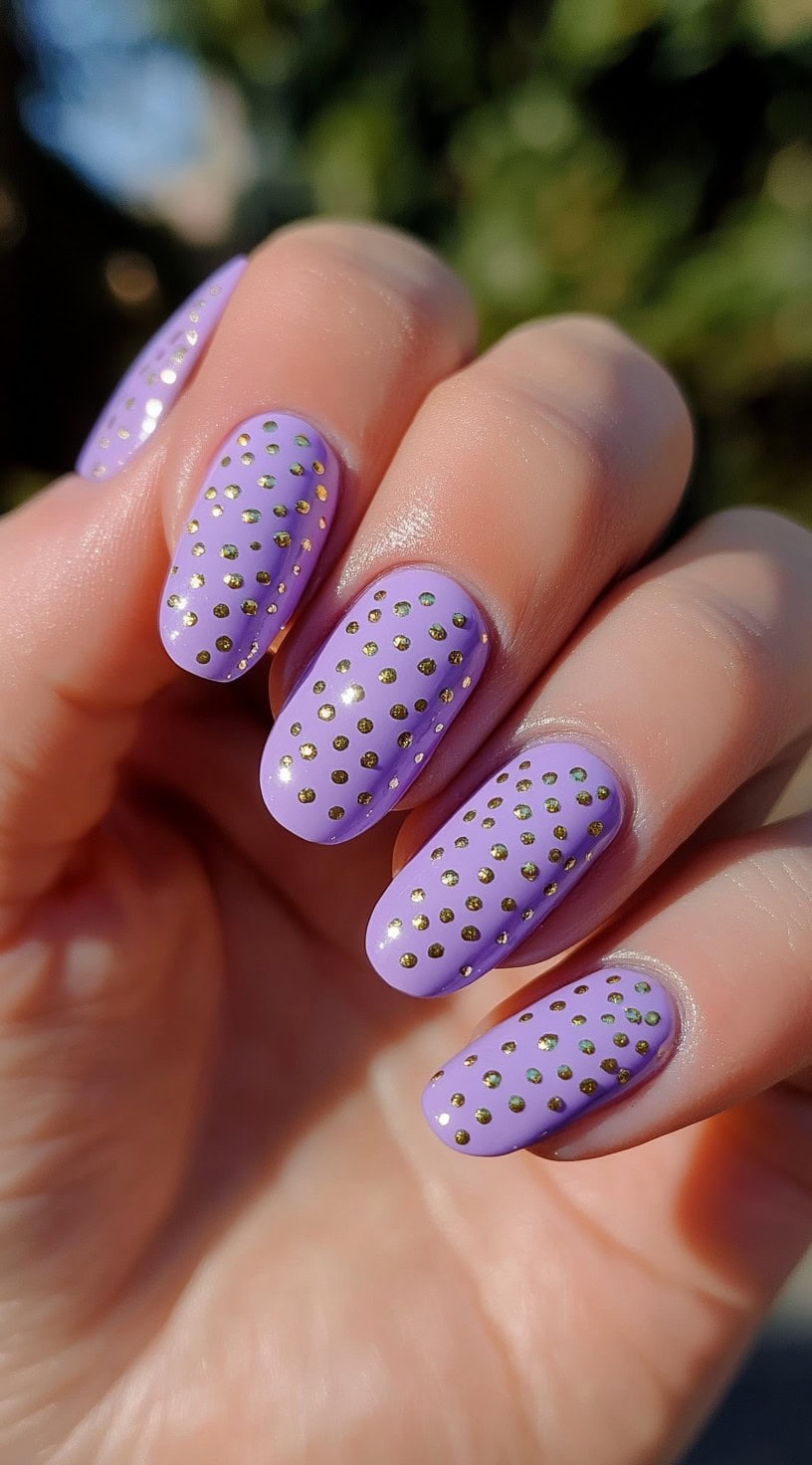 Oval nails painted in pastel lilac and covered evenly in small gold metallic dot studs.