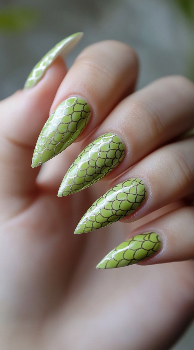 Stiletto nails painted in a vibrant lime matcha shade with a metallic dragon scale pattern stamped over each.