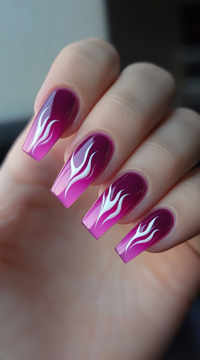 Long coffin nails with a fuchsia pink to purple ombre background and bold white flame art over each nail.