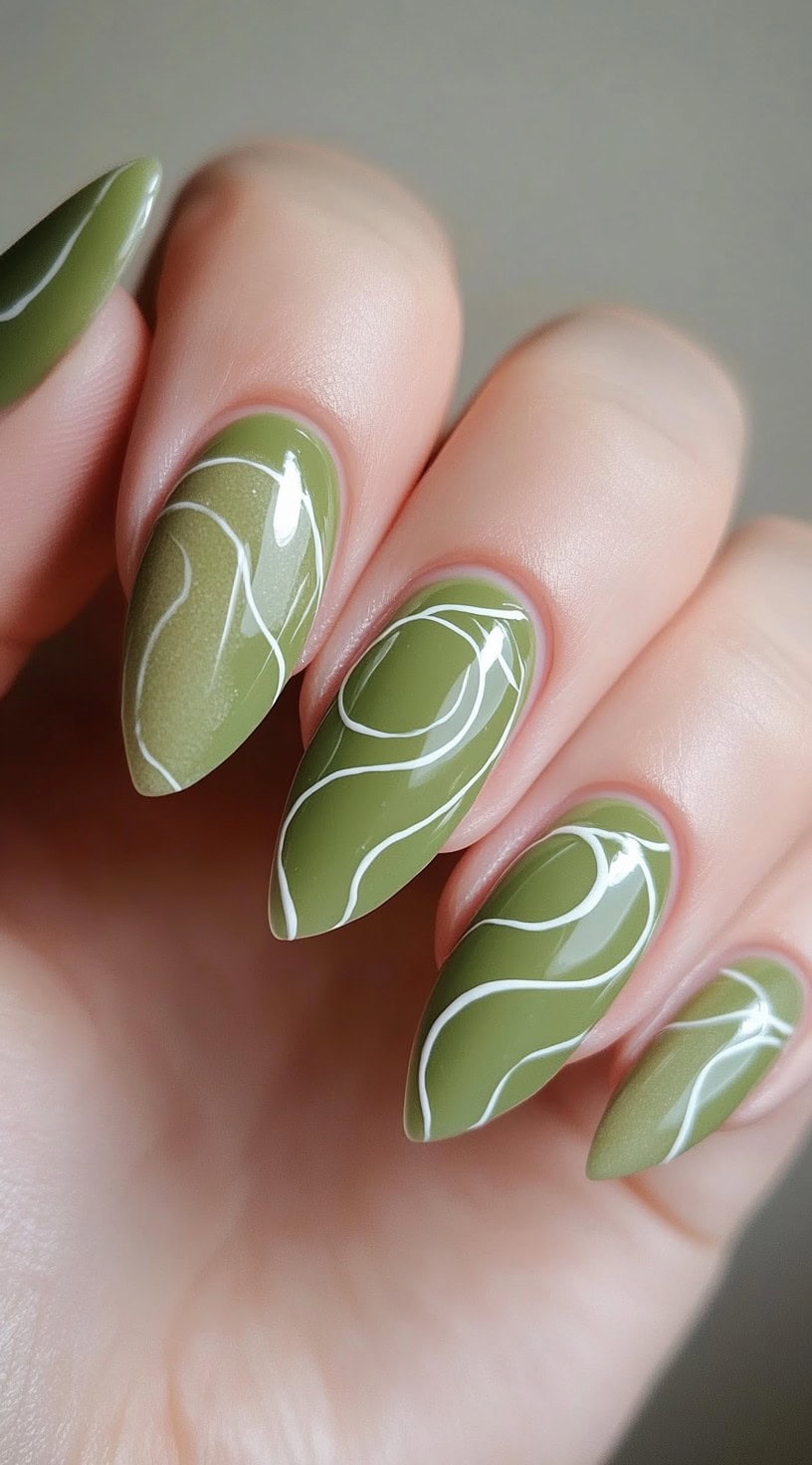 Almond-shaped nails painted in a soft matcha green with abstract white contour lines across each nail.