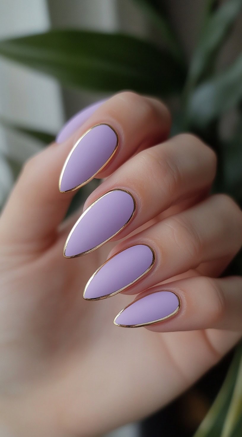 Almond-shaped nails painted in matte lilac with fine metallic gold chrome outlining each nail.
