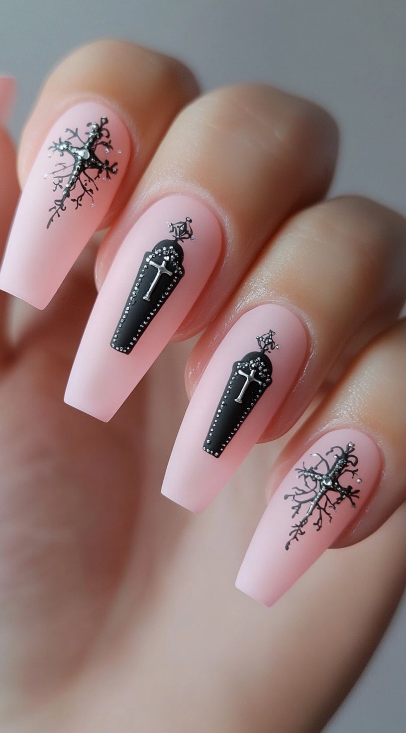 Matte pink coffin nails featuring black coffin graphics with cross embellishments and gothic branches.