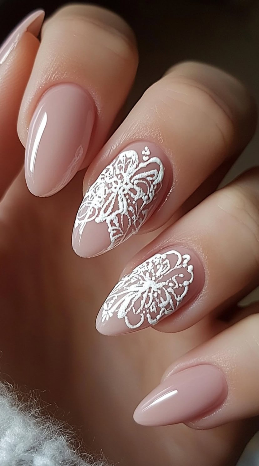 A hand with soft mauve almond-shaped nails, two of which display intricate white butterfly lace designs.