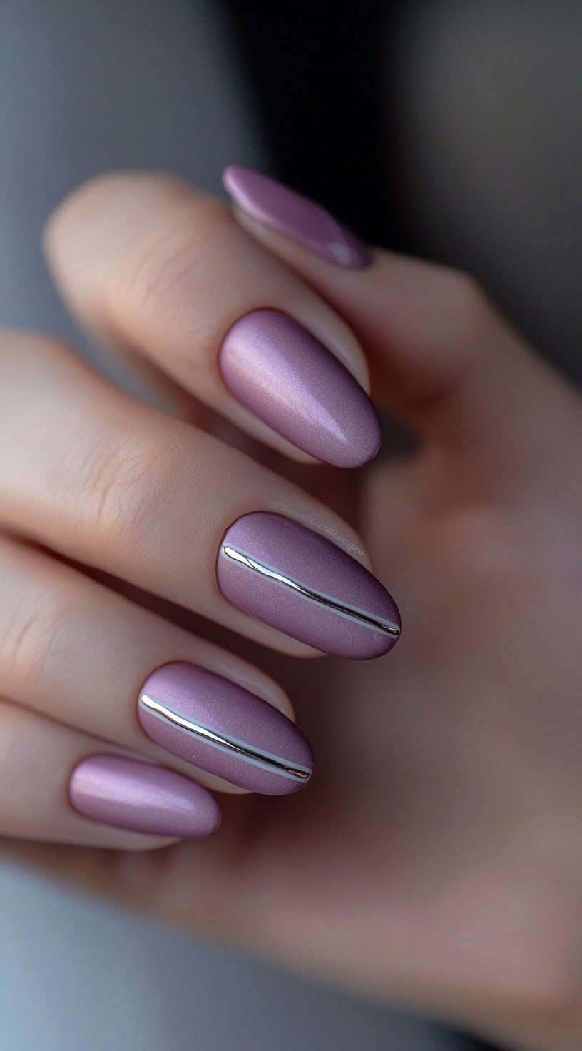 A hand with almond-shaped mauve satin nails, each featuring a single metallic chrome line down the center.
