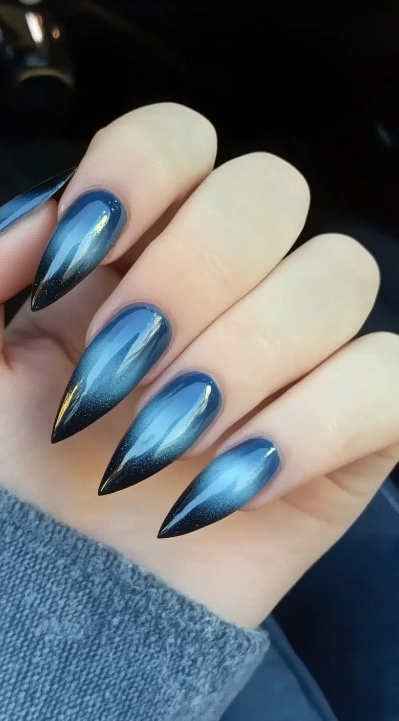 A set of stiletto nails with a smooth gradient transitioning from deep midnight blue to black, finished with a glossy shine.