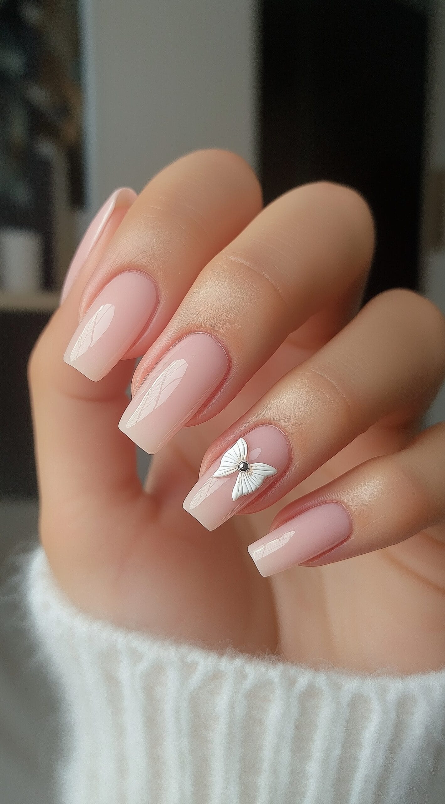 A hand with squoval milky pink nails and a 3D white butterfly charm on the ring finger.