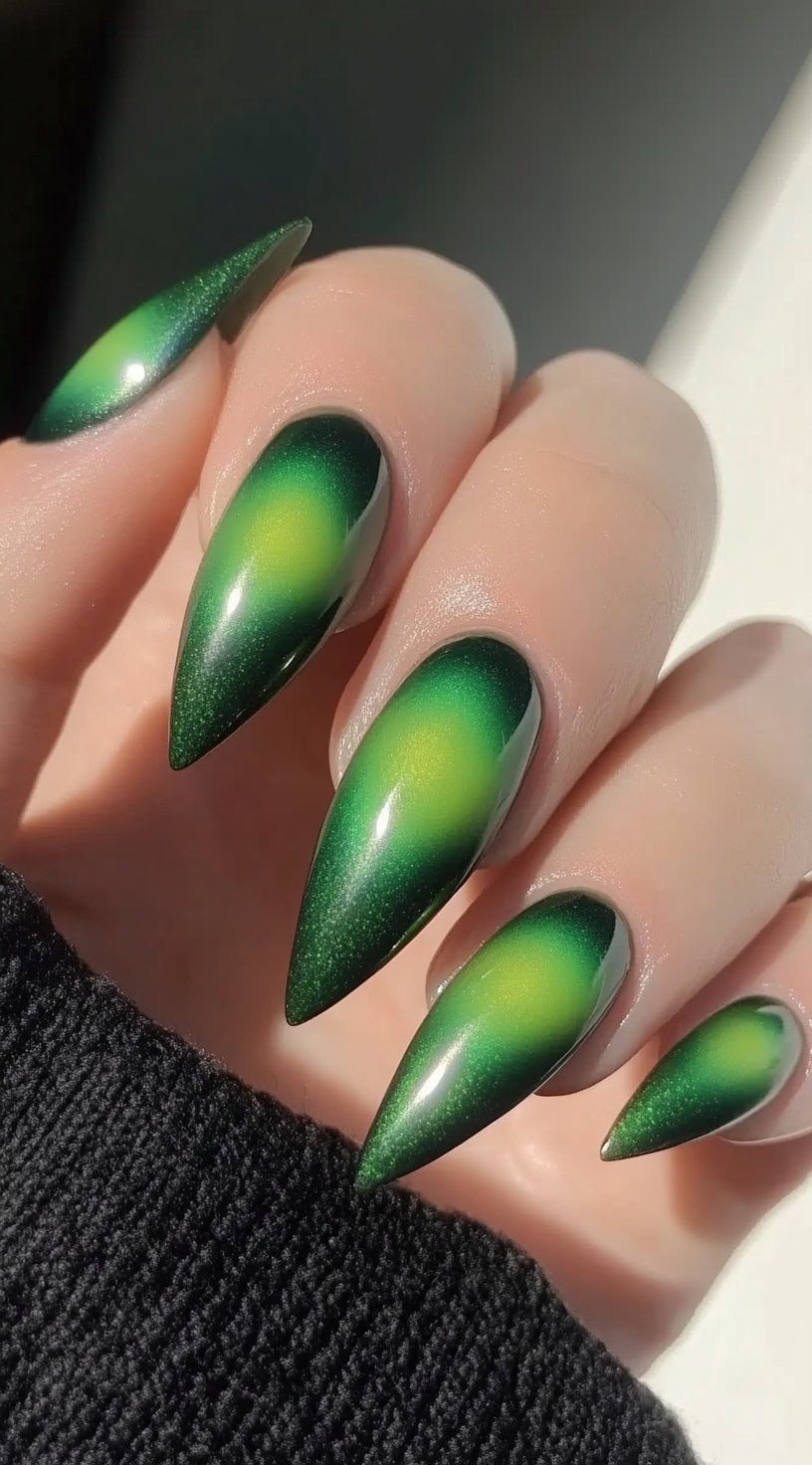 A close-up of stiletto-shaped nails featuring a neon green aura effect with a glowing yellow-green center.