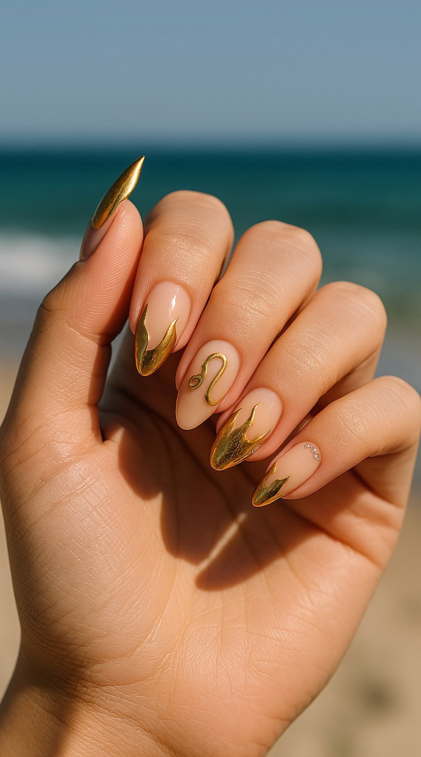 Hand with nude almond nails featuring gold foil flame tips and the Leo zodiac symbol on the ring finger.