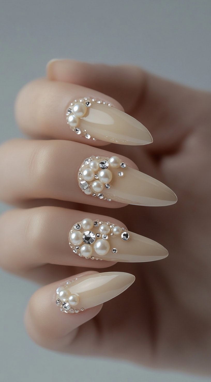 A set of nude almond-shaped nails adorned with clusters of pearls and sparkling crystals, creating an opulent and elegant design.