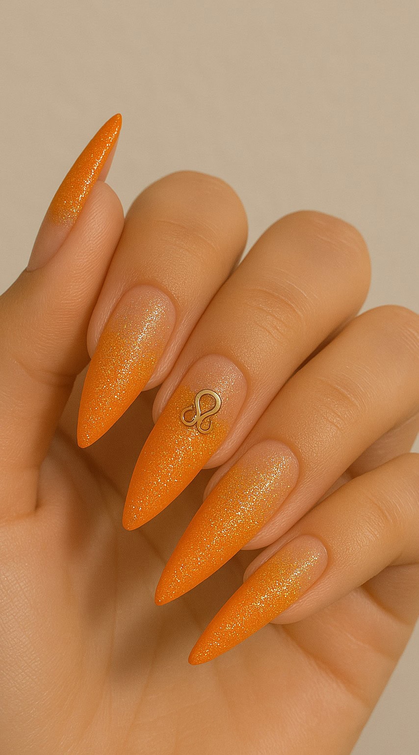 Bright orange stiletto nails with a subtle glitter gradient and a small gold Leo symbol charm.