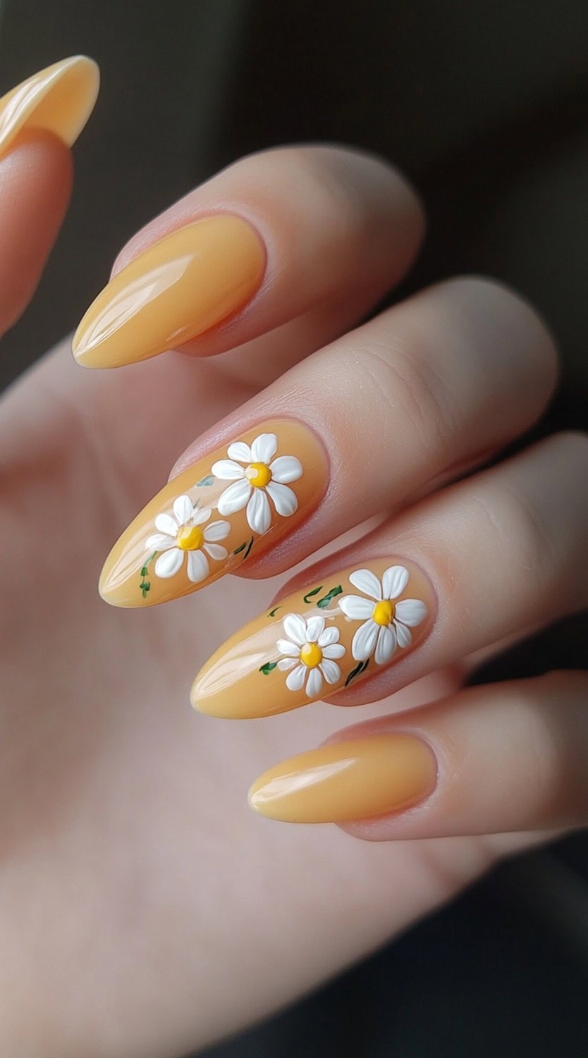 A hand with pastel yellow almond-shaped nails, two of which are decorated with detailed white daisy flower art.