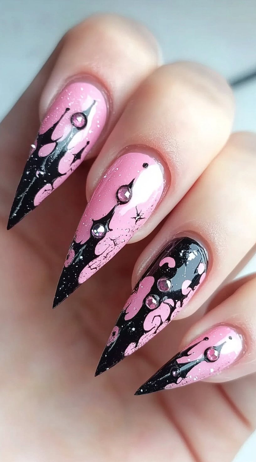 Pink stiletto nails with black drip designs and rhinestones on each nail.
