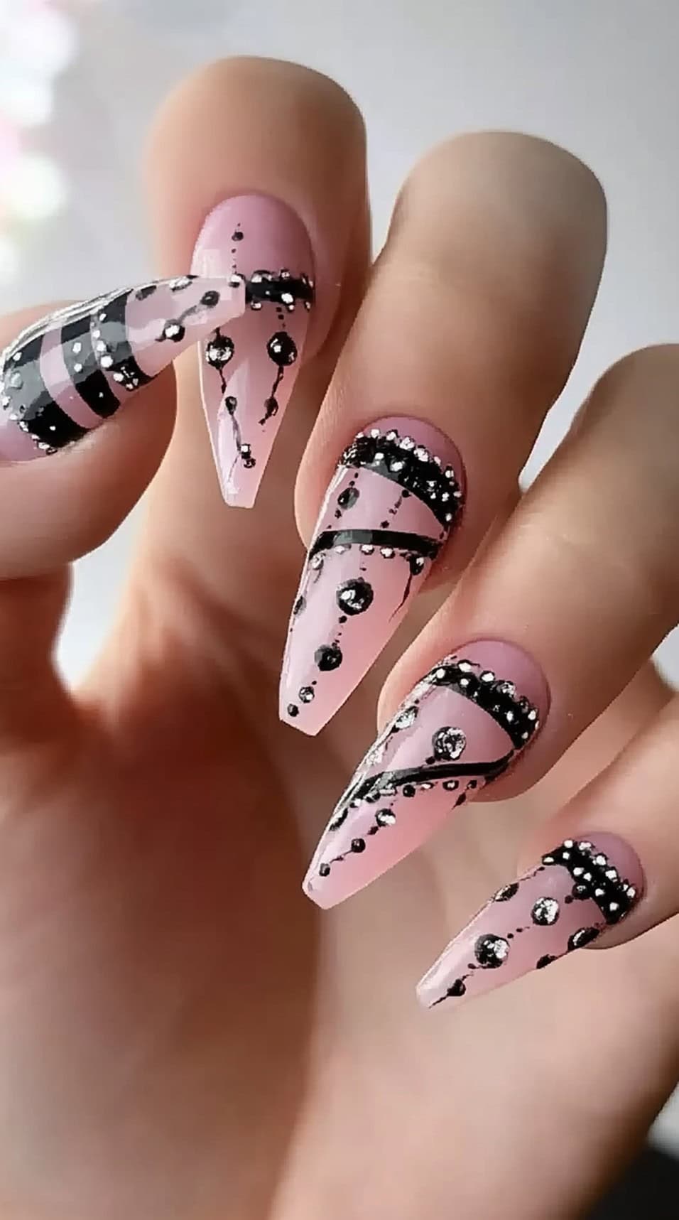 Pink tapered square nails decorated with black lines, crystals, and draped gem-like accents in a gothic motif.