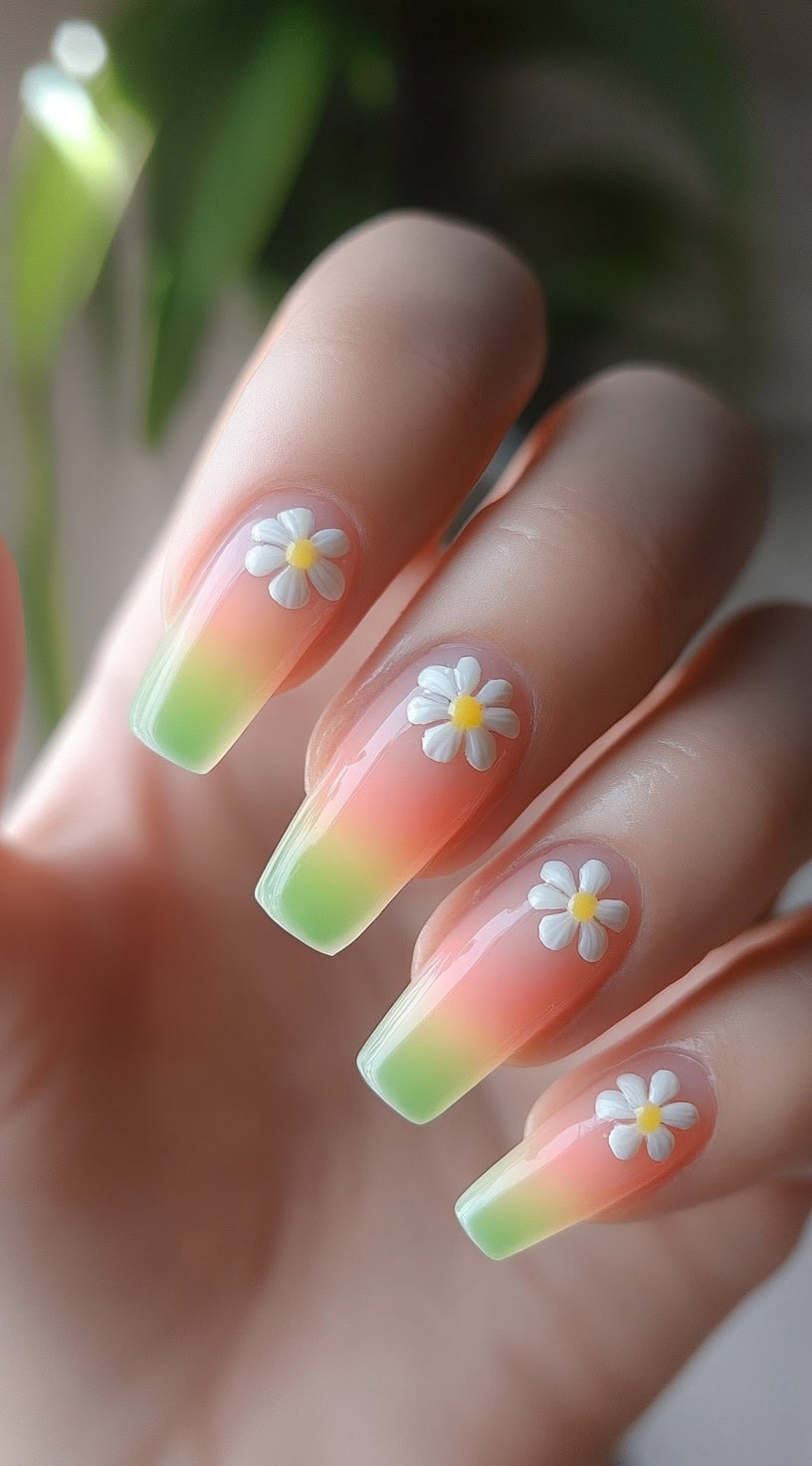 A hand with pink and green ombre square nails decorated with 3D white daisy flower accents.