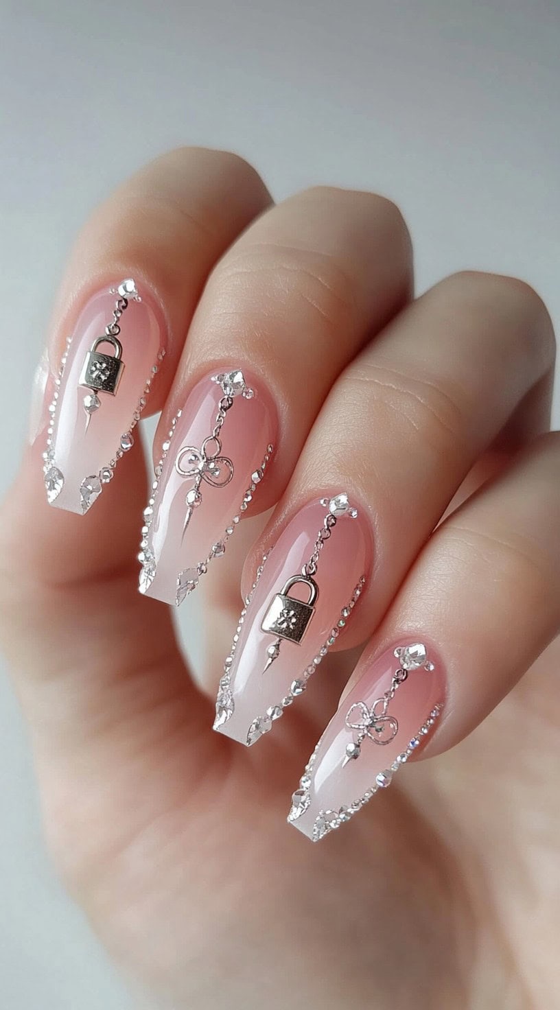 Long pink nails with rhinestones, silver lock charms, and key motifs.