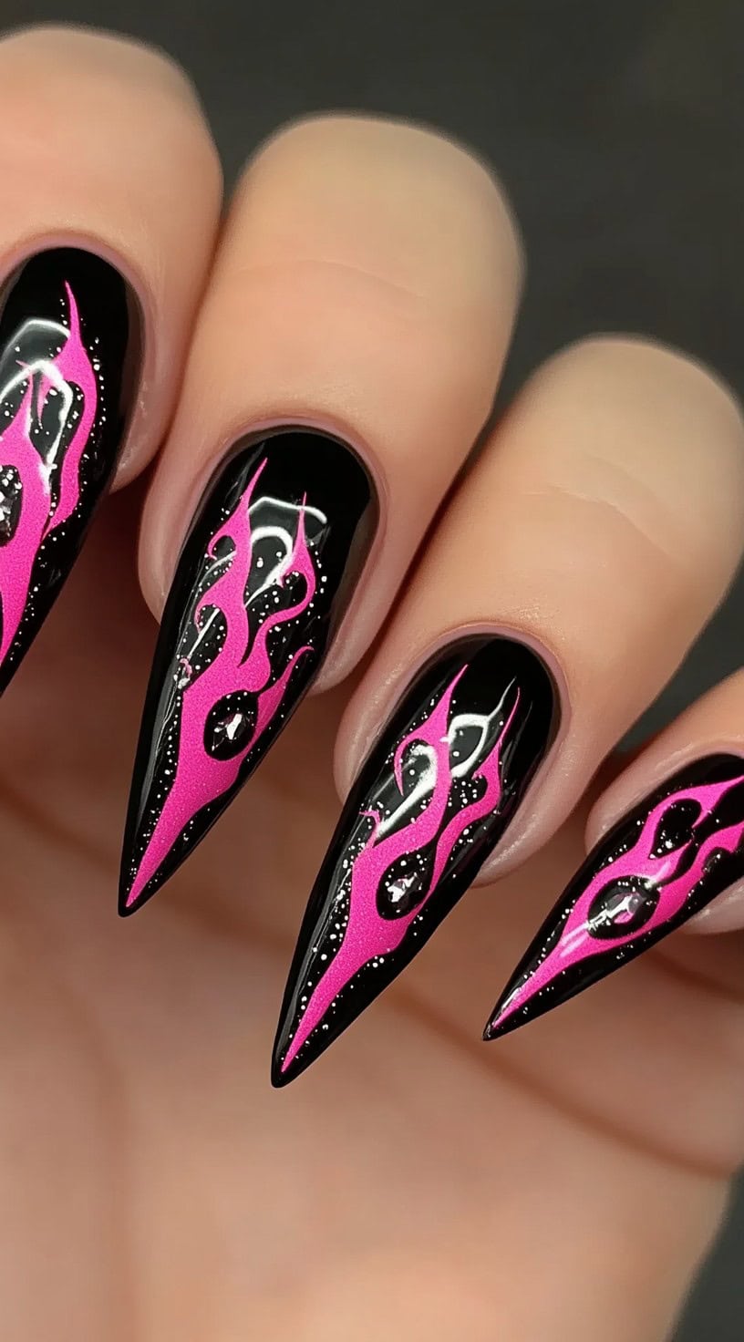 Stiletto nails with a glossy black base and hot pink flame designs accented by rhinestones.