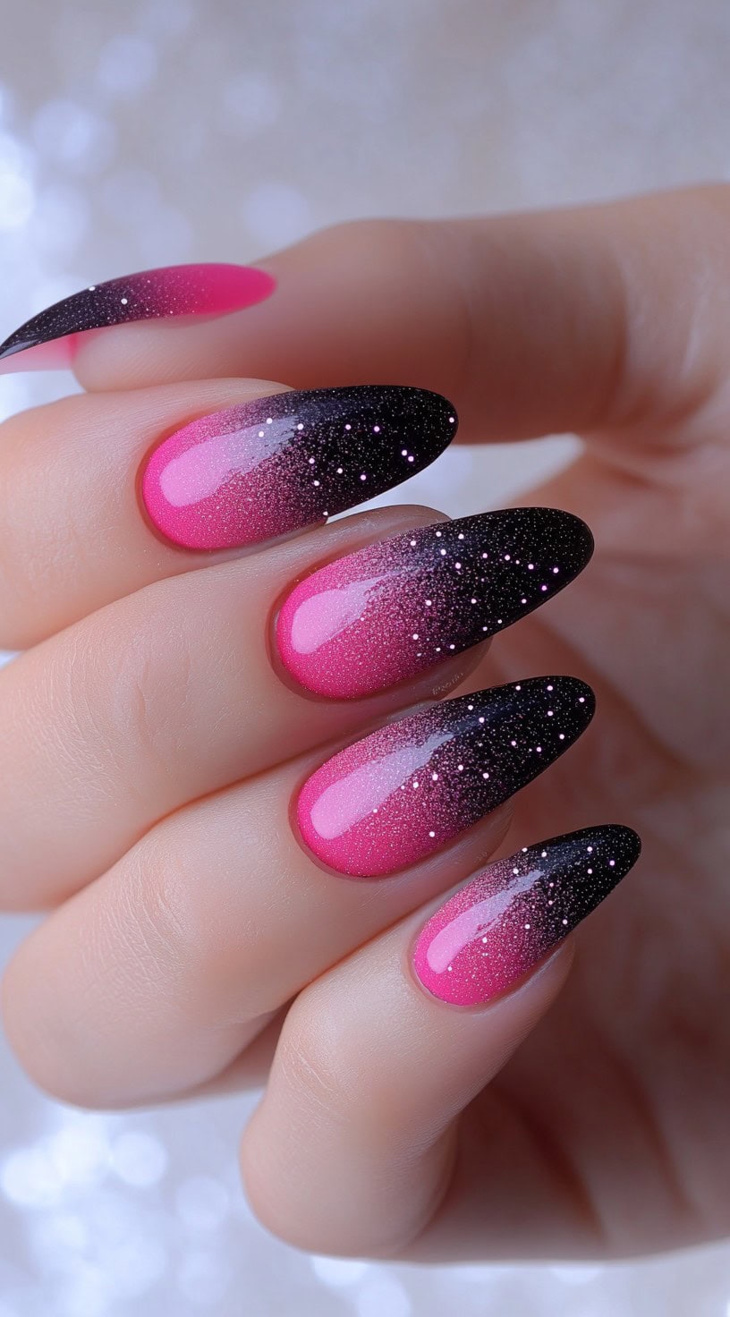 Almond-shaped nails featuring a vibrant pink-to-black ombre coated with fine white and pink glitter for a starry night effect.