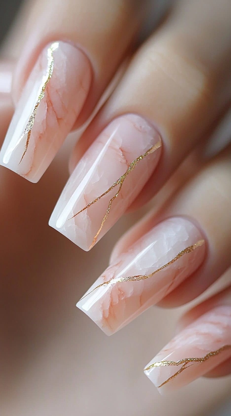A hand with long square nails featuring a soft pink marble pattern detailed with fine gold veining.