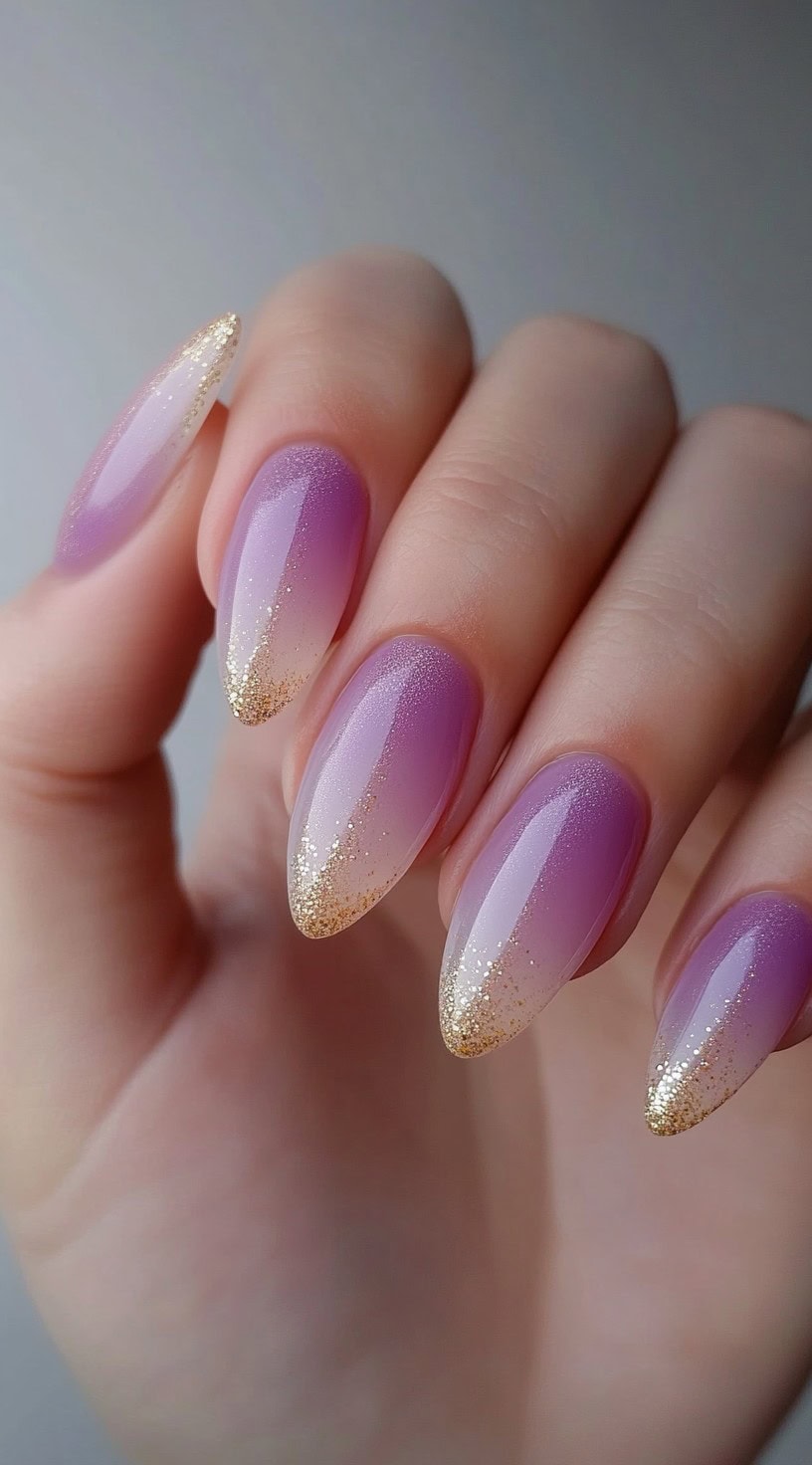 Almond-shaped nails fading from soft pink to lilac, finished with delicate gold glitter at the tips.