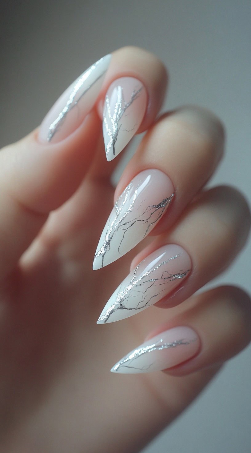 A hand with pointed nails in a soft pink-to-white ombré, overlaid with thin silver lines resembling delicate tree branches.
