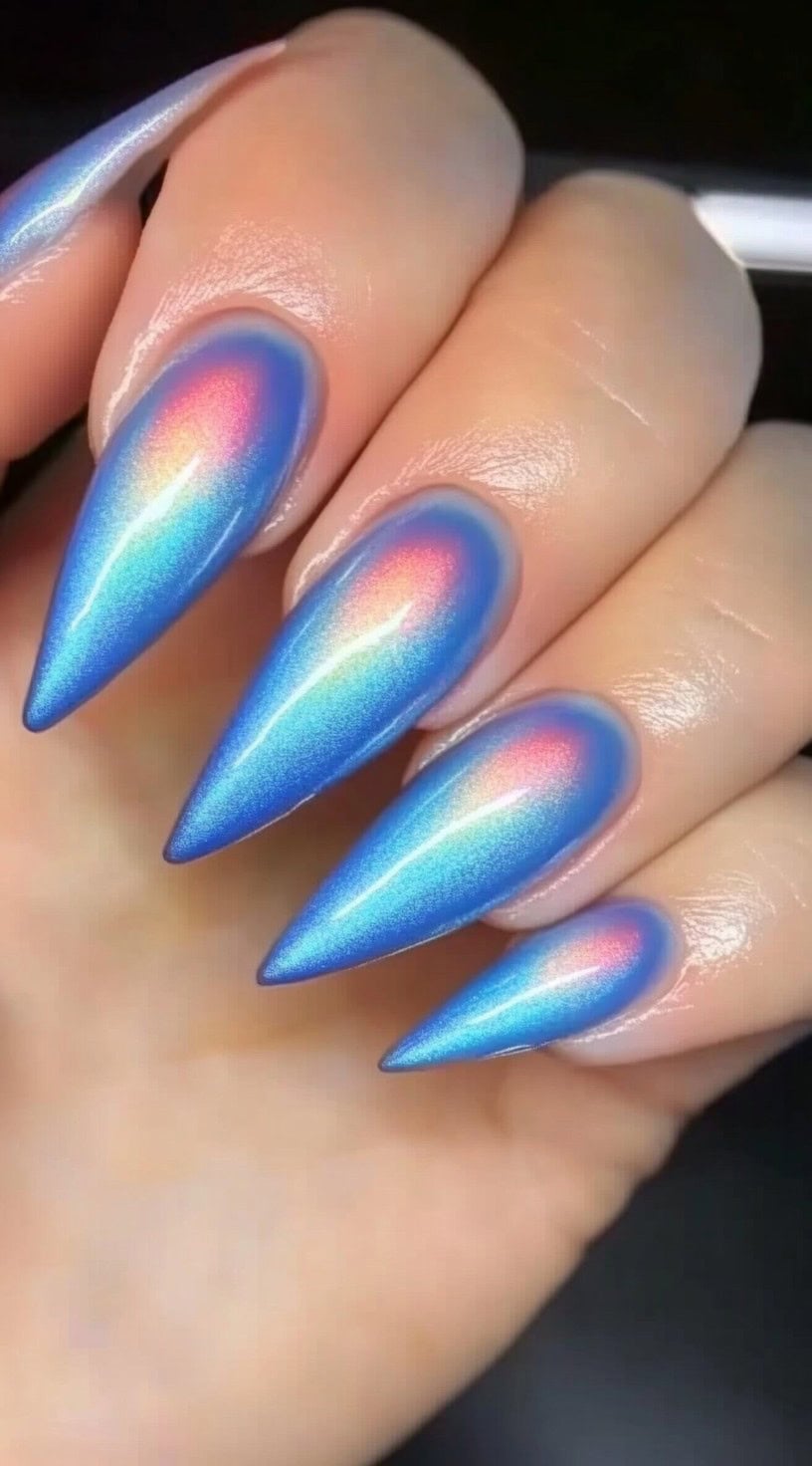 Stiletto nails with a metallic blue aura effect, accented by glowing pink and orange iridescent shifts.