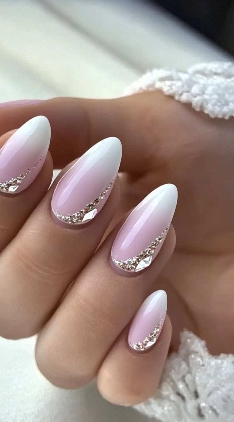 Elegant almond-shaped French ombre nails adorned with sparkling rhinestones arranged in a diagonal pattern.