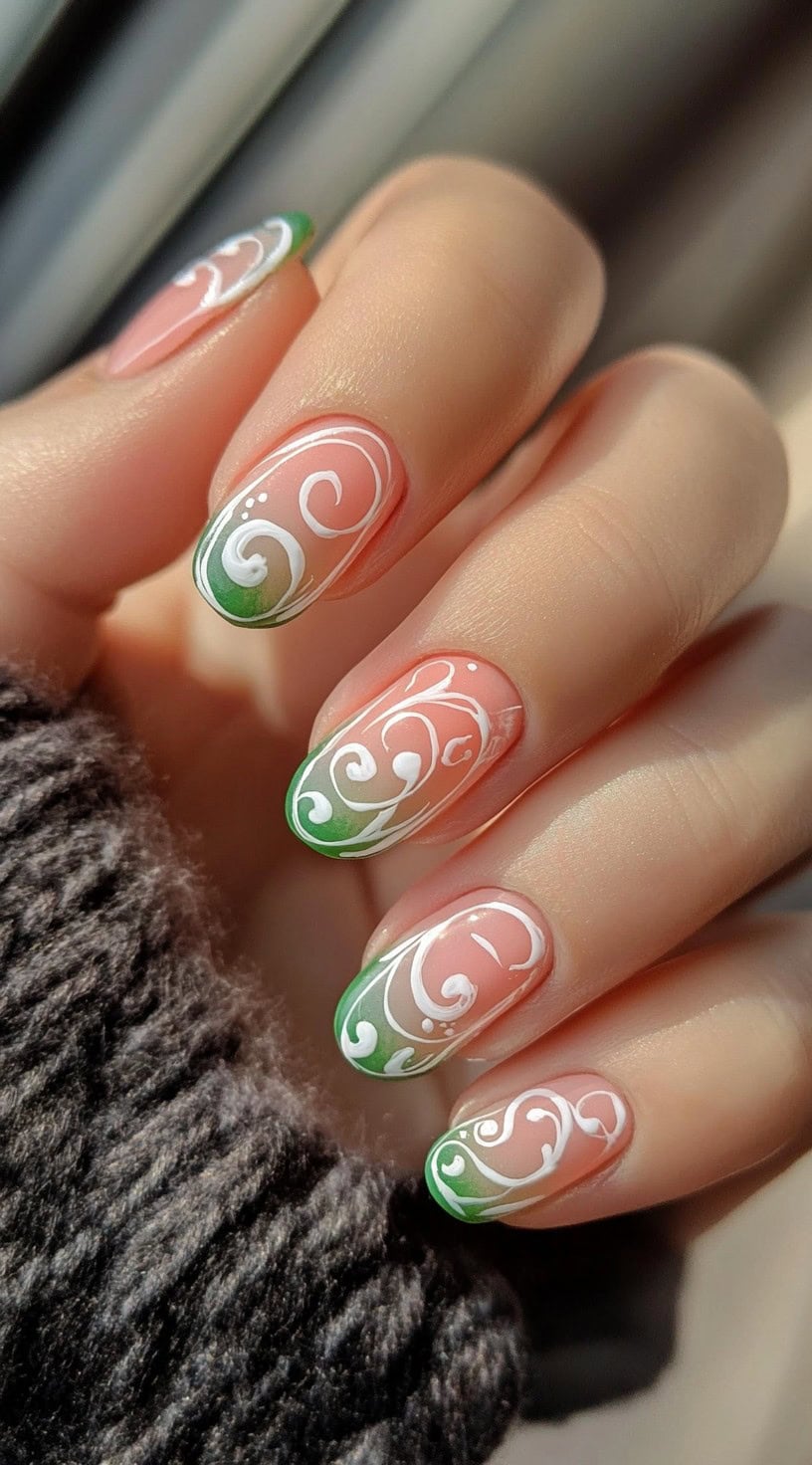 Round-shaped nails with a pink and green ombre base and elegant white swirl detailing across the top.