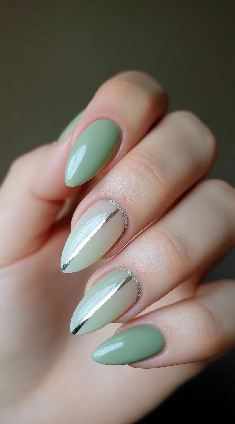 Almond-shaped nails in a sage green and sheer nude mix, detailed with metallic silver lines along the cuticle and nail center.