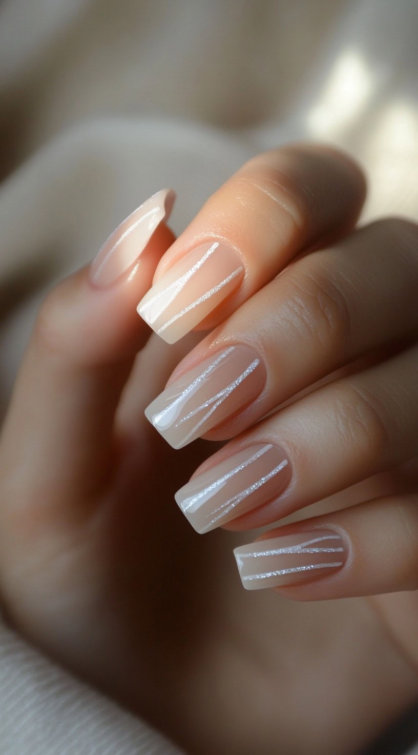 A hand with square nails in a sheer nude base, decorated with thin silver diagonal stripes.