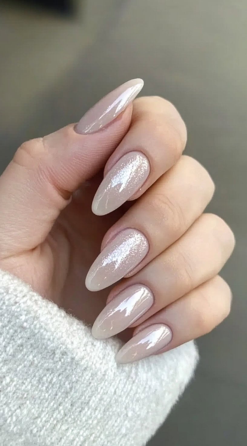 A close-up of long almond-shaped nails with a sheer nude base and a soft dusting of fine glitter.