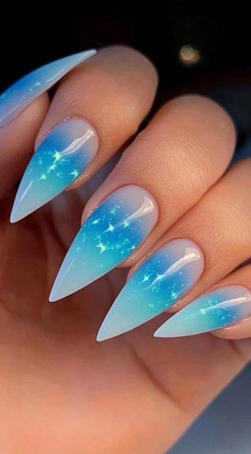 Stiletto nails featuring a soft pastel blue aura that fades into a translucent base, accented with tiny glowing sparkles.
