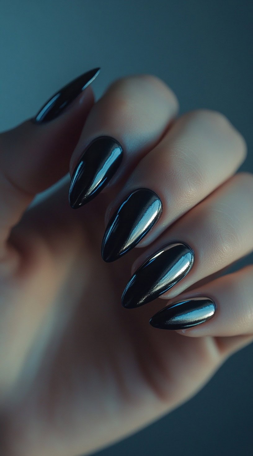 A set of almond-shaped nails with a deep black chrome finish, reflecting light for a mirror-like effect.
