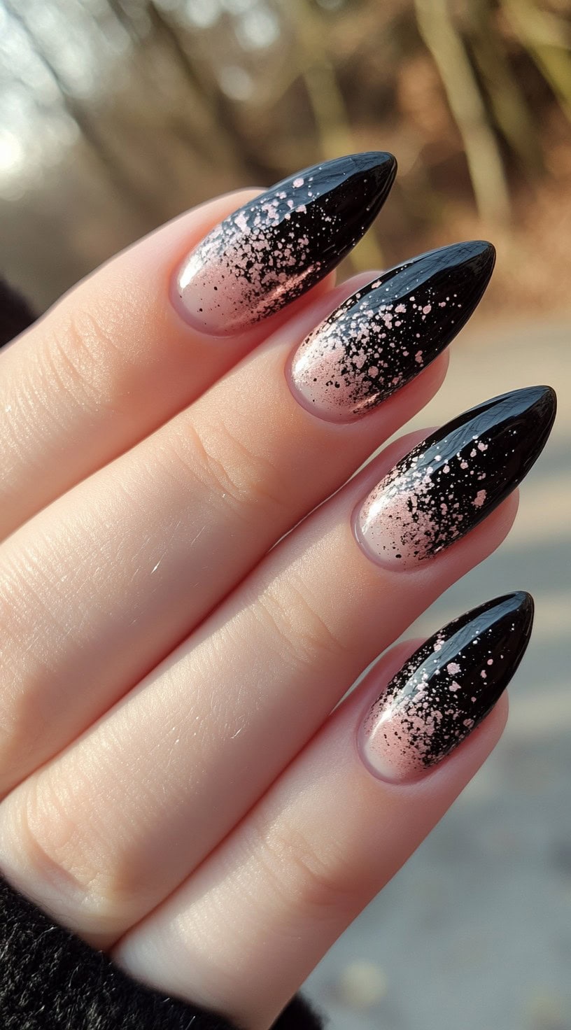 Almond nails showing a nude base transitioning into black with a pink paint-splatter effect layered over the fade.