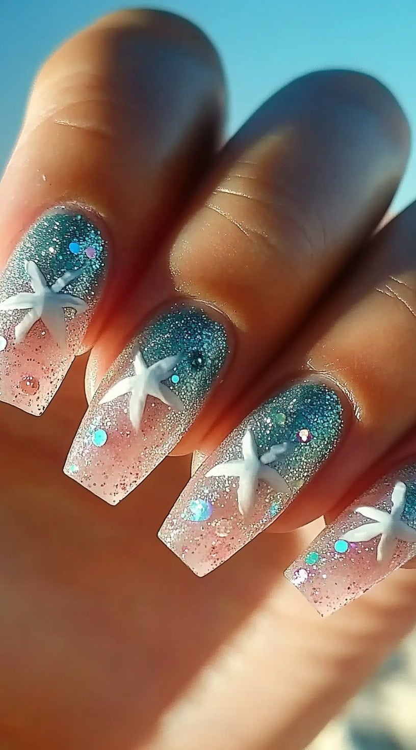 Square-shaped nails with a glittery blue-to-pink gradient base and 3D white starfish accents.