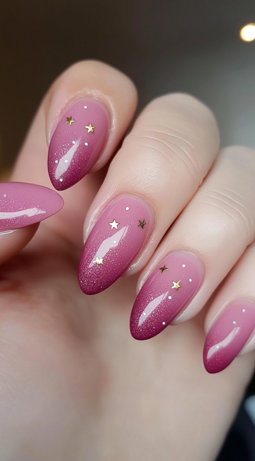 Almond nails with a pink ombre fade and fine shimmer, embellished with tiny gold stars and white dots.