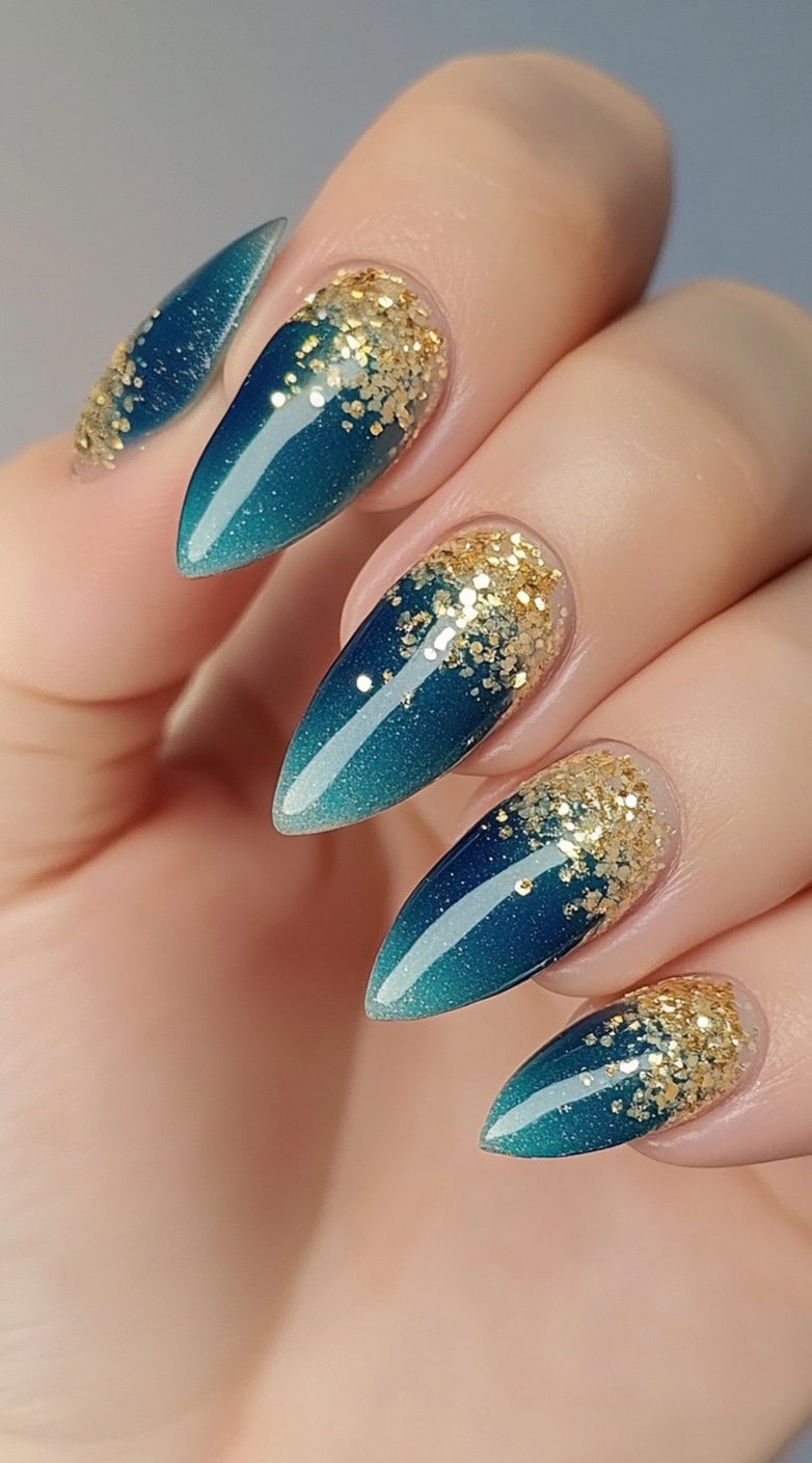 Almond nails with a teal to deep blue ombre and heavy gold glitter packed near the cuticle.