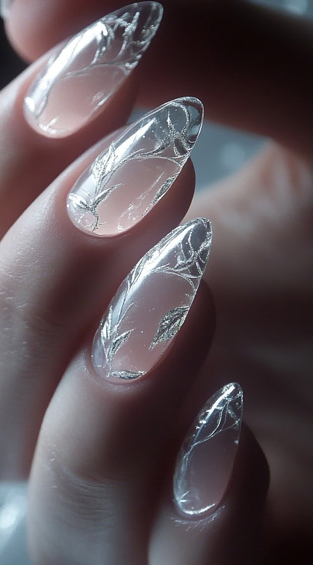 A set of fully transparent almond-shaped nails decorated with delicate silver leaf patterns, giving a modern and ethereal appearance.
