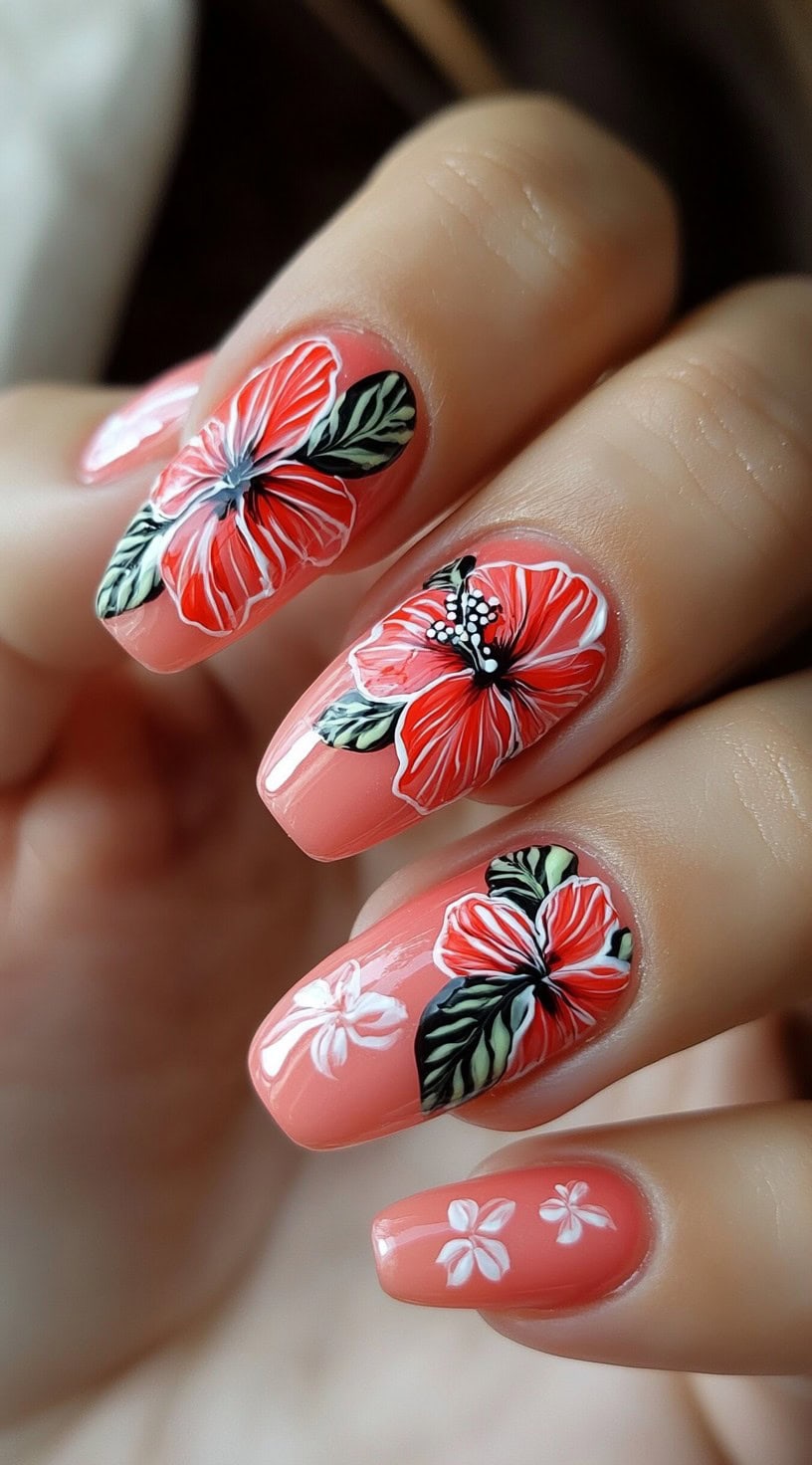 Rounded nails with a coral pink base featuring detailed hibiscus flowers in vivid red and green leaves.