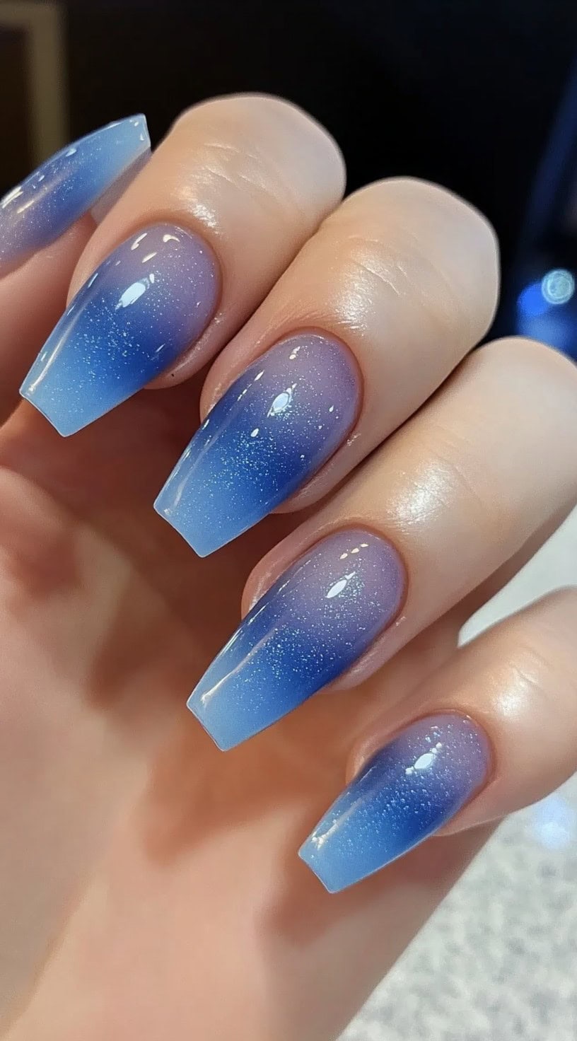 Coffin-shaped nails featuring a soft blue-to-purple aura ombré, speckled with fine glitter for a celestial shimmer.