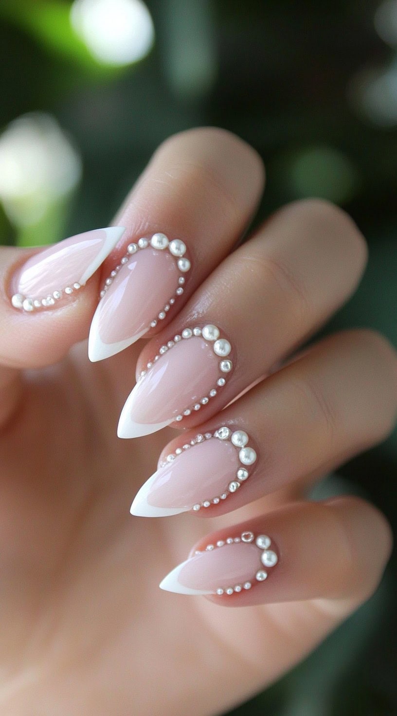 A set of almond-shaped nails with nude-pink bases, crisp white tips, and dainty pearl embellishments forming curved outlines.
