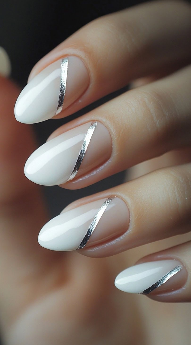 A close-up of oval-shaped nails with white diagonal tips and thin metallic silver striping.